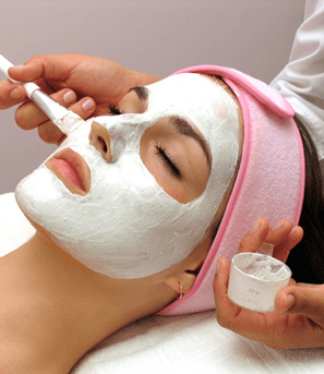 Косметолог кисточкой наносит маску на лицо женщины
